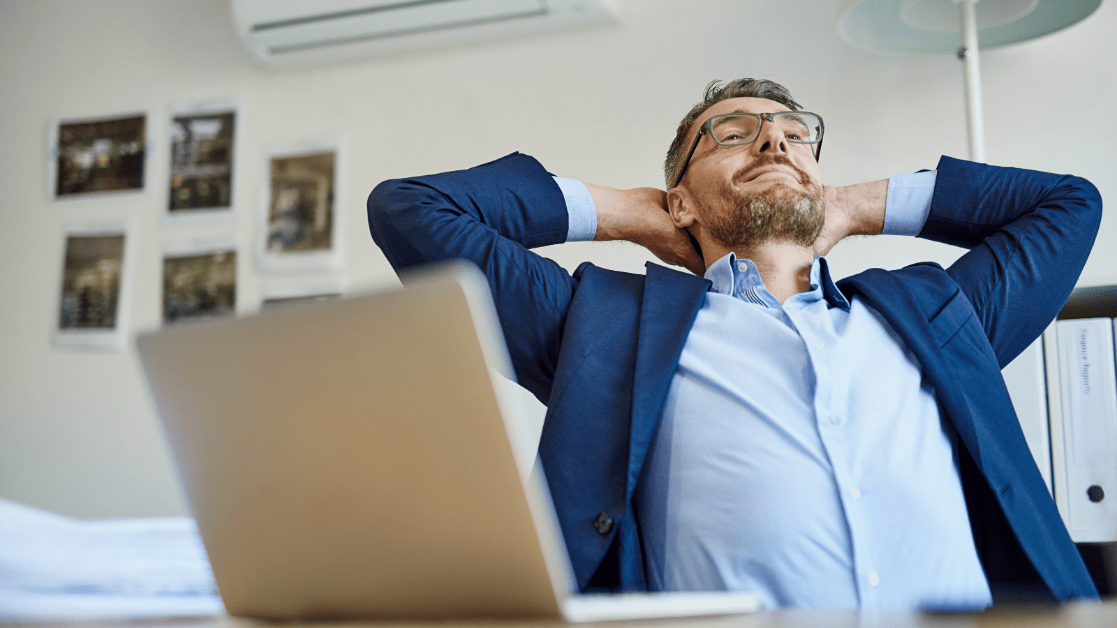 A man in a suit sits at a desk with his laptop open